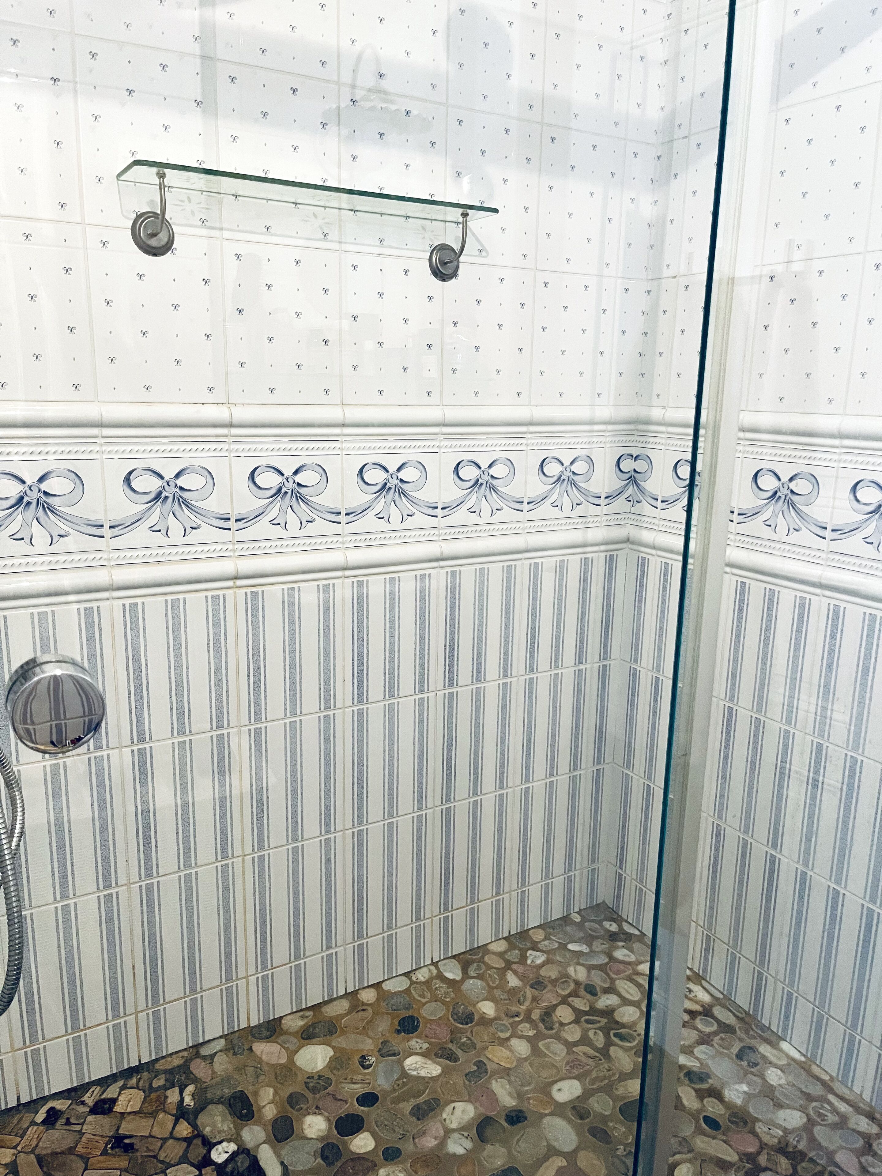Eine Dusche mit Glastür, Fliesenwänden mit floralem Muster und einem Boden mit Kieselsteindekor.