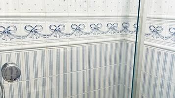 Eine Dusche mit Glastür, Fliesenwänden mit floralem Muster und einem Boden mit Kieselsteindekor.