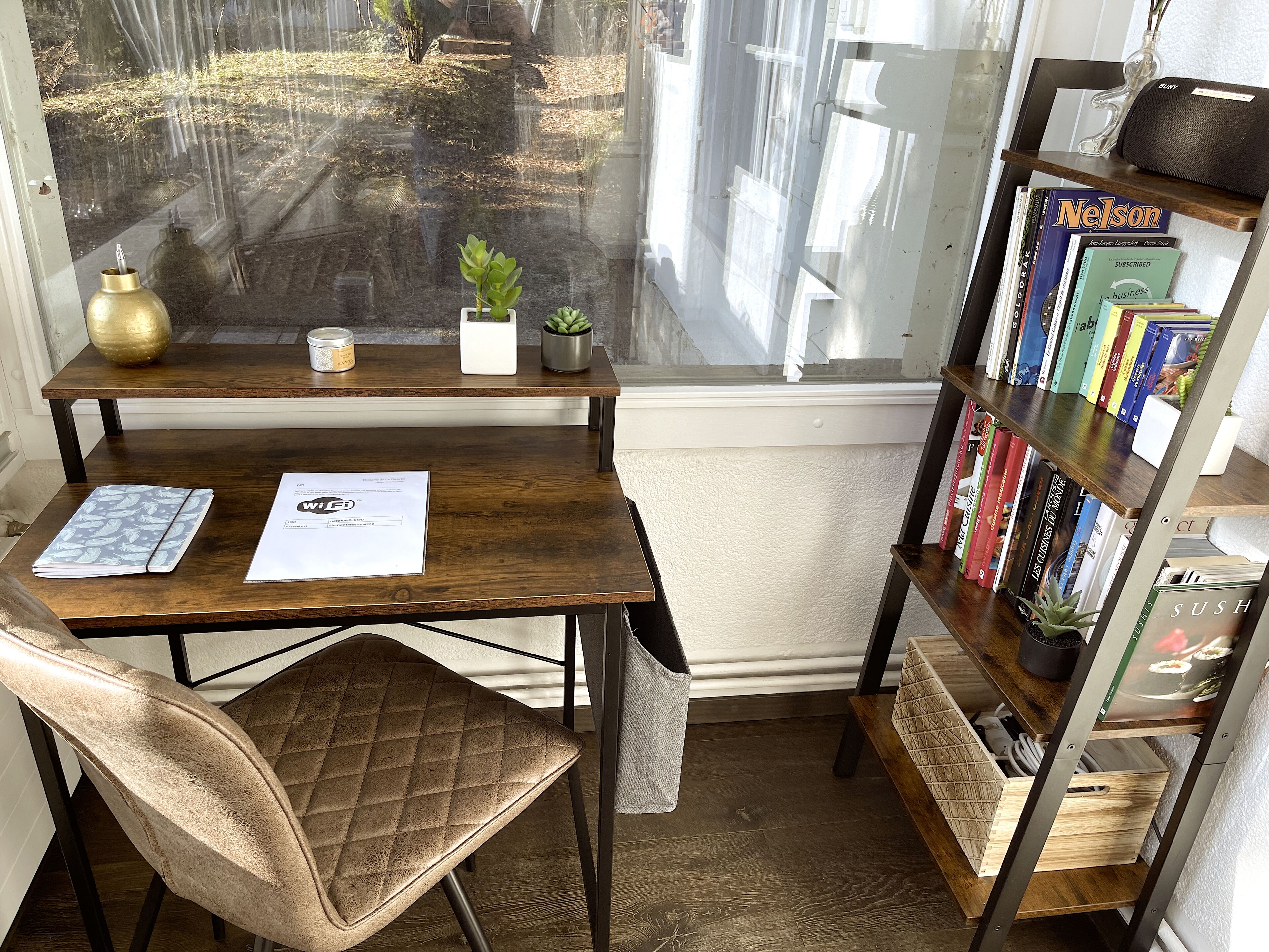 Un bureau en bois, une chaise, une bibliothèque et une fenêtre donnant sur un jardin.