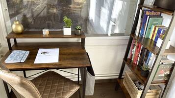 Ein Holztisch mit einem Stuhl, einem Bücherregal und einem Fenster mit Blick auf einen Garten.