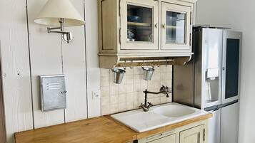 Eine Küche mit Holzarbeitsplatte, Spüle, einem Küchenschrank im Vintage-Stil mit Glastüren, einer Wandleuchte und einem Kühlschrank.