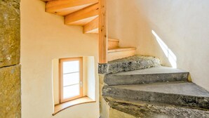 Una escalera de caracol con escalones de piedra y barandillas de madera, que conduce a una pequeña ventana con una puerta.