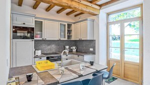 Cocina moderna con armarios blancos, un refrigerador Bosch, un lavamanos y una cafetera. Hay sillas azules y un escurreplatos amarillo.