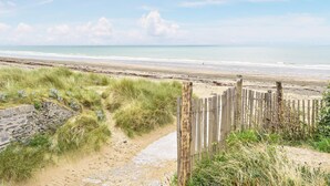 Una playa arenosa con una valla de madera y dunas cubiertas de hierba.