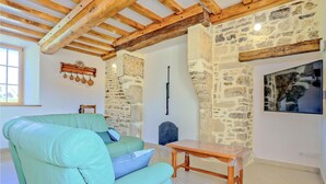 Una habitación con pared de piedra, vigas de madera, un sofá verde, una mesa de madera y un cuadro colgado.