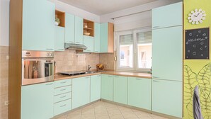A kitchen with teal cabinets, a stainless steel oven, and a window with blinds. - Pet friendly apartment in Podstrana with WiFi (Podstrana)