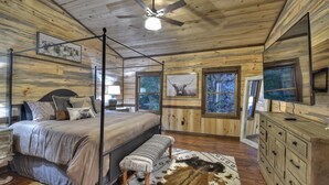 A bedroom with a four-poster bed, a ceiling fan, and a large window with a view of trees.