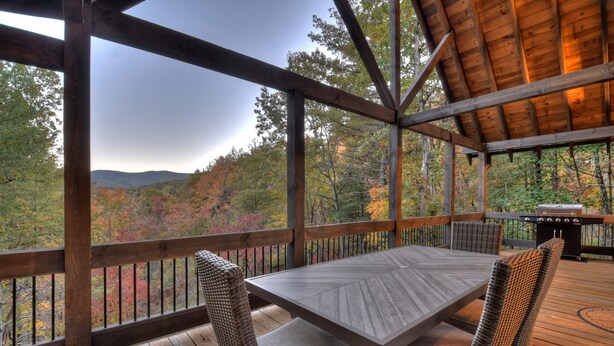 A wooden deck with a table and chairs, overlooking a forested landscape.