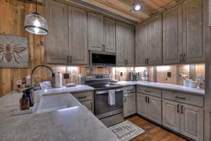Una cocina con gabinetes de madera, horno de acero inoxidable, microondas y un lavamanos.