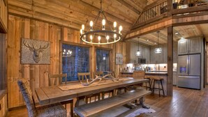 A wooden interior with a dining table, benches, and a chandelier.