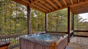 A wooden hot tub on a deck with a view of autumn trees.