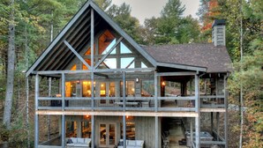 A multi-level wooden cabin with balconies, large windows, and a fireplace.