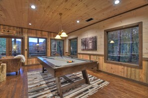 Una mesa de billar en una habitación con paredes de madera y ventanas amplias.