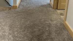Ein schmaler Flur mit Teppichböden, der zu einem Schlafzimmer mit Bett und Fenster führt.