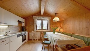 A cozy kitchen with wooden cabinets, a dining area with a table and benches, and a window with curtains. - traditionelles Ferienh. Soell (Söll)