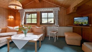 A cozy cabin interior with a wooden ceiling, a sofa, a dining table with a vase, a chair, a television, and a window with curtains. - traditionelles Ferienh. Soell (Söll)