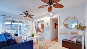 A spacious living area with a blue sofa, a dining table, and a ceiling fan.
