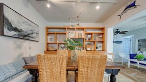 A dining area with a wooden table, woven chairs, and a decorative shelf with various items.
