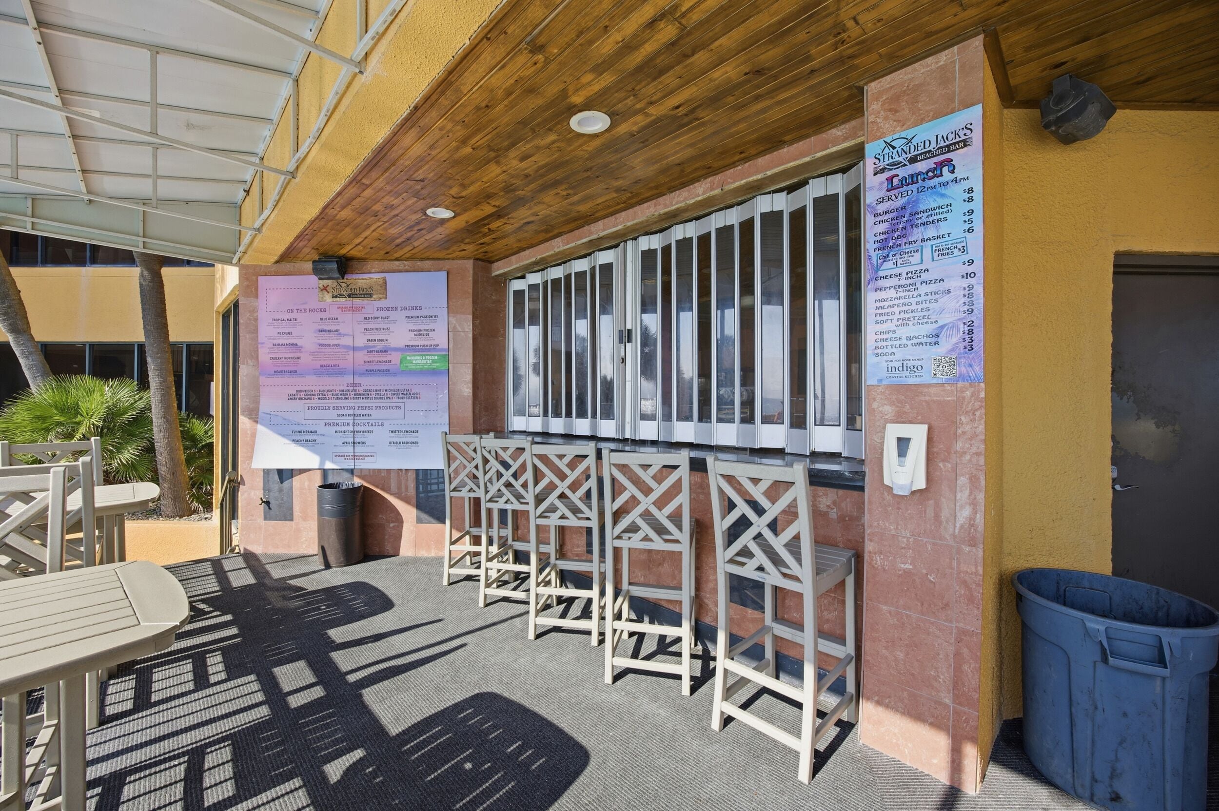An outdoor seating area with wooden tables and chairs, a menu board, and a trash bin.