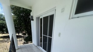 Un balcon doté d’un sol carrelé, d’une rambarde en métal et d’une porte-fenêtre coulissante donnant sur un espace extérieur abrité.