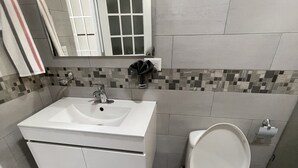 Une salle de bain avec un lavabo blanc, un miroir et des toilettes.