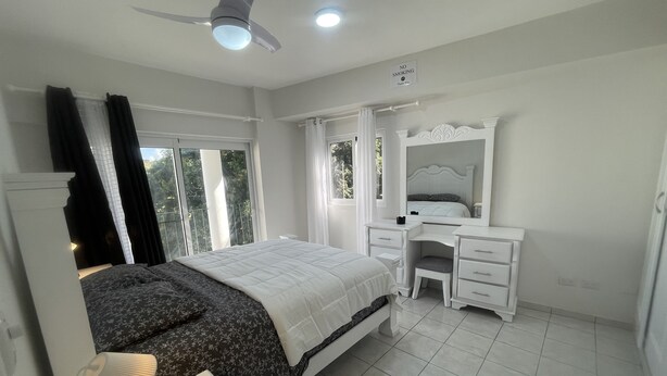 Une chambre à coucher comprenant un lit, un bureau, une chaise, un miroir et un ventilateur de plafond.