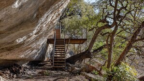 Eine Holztreppe führt zu einer Plattform in einer natürlichen Umgebung mit Bäumen und Felsen.
