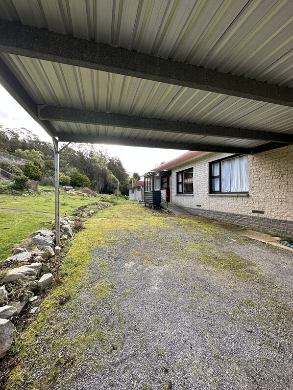 A covered outdoor area with a gravel path leading to a building with a stone exterior and a red roof.