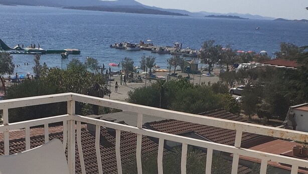 Une terrasse avec une table et des chaises, donnant sur une zone côtière où l’on peut voir des bateaux et des gens.