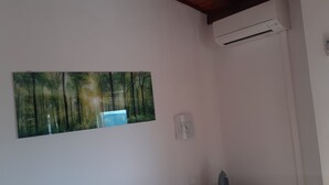Une pièce dotée d’un climatiseur fixé au mur, d’un tableau représentant une scène de forêt et d’une petite prise électrique.