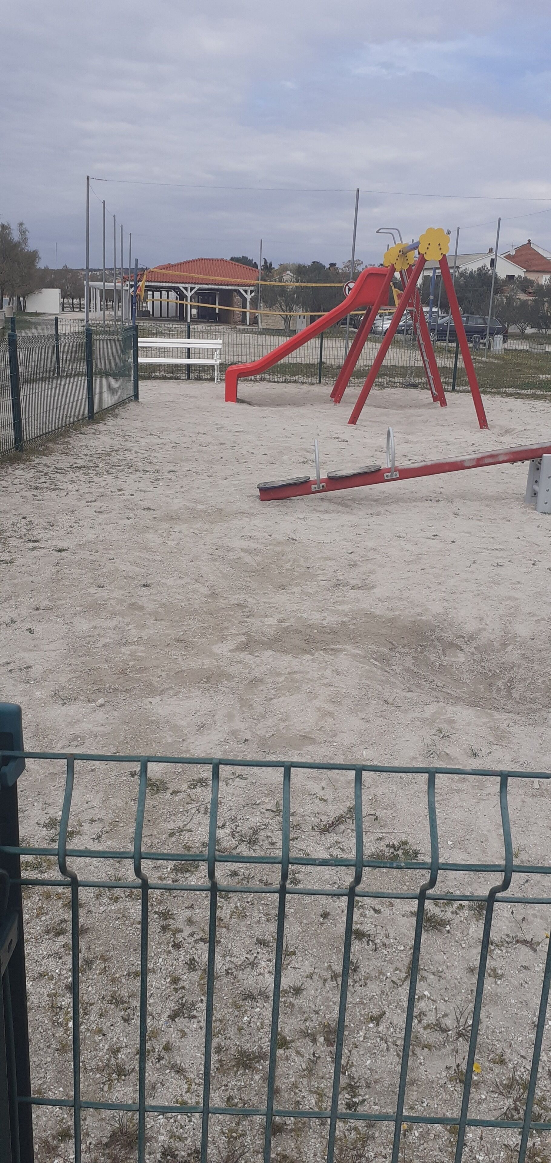 A playground with a red slide and swings, surrounded by a fence.