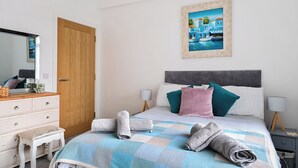 A bedroom with a bed, a dresser, a mirror, a painting, and a nightstand. - Mary Bowes Terrace (Bournemouth)