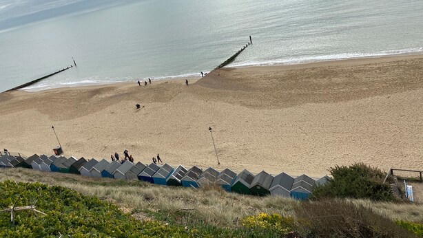 A beach with a wooden jetty and beach huts in the foreground. - Mary Bowes Terrace (Bournemouth)