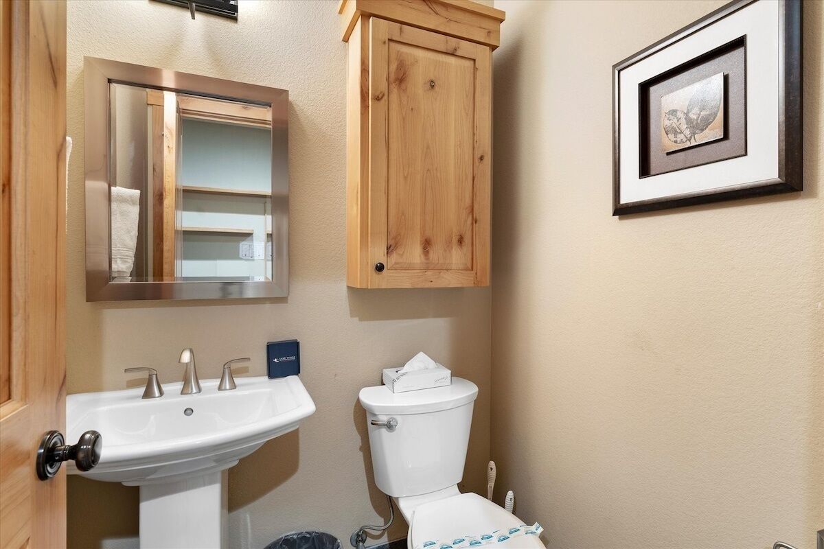 A bathroom with a white sink, a toilet, and a wooden cabinet above the toilet.