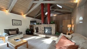 A cozy living room with a stone fireplace, a sofa, a coffee table, and a television. - Tumbleweed Pines 3 Bedroom Home by RedAwning (Incline Village)
