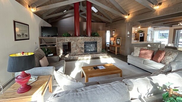 A spacious living room with a stone fireplace, wooden beams, and a television on a stand. - Tumbleweed Pines 3 Bedroom Home by RedAwning (Incline Village)