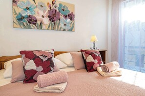Una habitación de hotel con una cama, almohadas, una lámpara y un cuadro de flores en la pared.