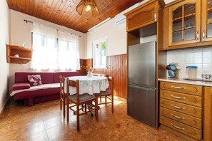 Cozinha compacta com armários de madeira, geladeira e área de refeições com mesa e cadeiras.