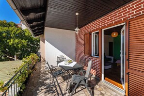 Um pátio externo com mesa e cadeiras, uma parede de tijolos e uma porta de vidro deslizante que dá para um espaço interno.