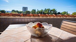 A table with a decorative bowl containing fruit, set against a tiled wall with a view of trees and a building in the distance.