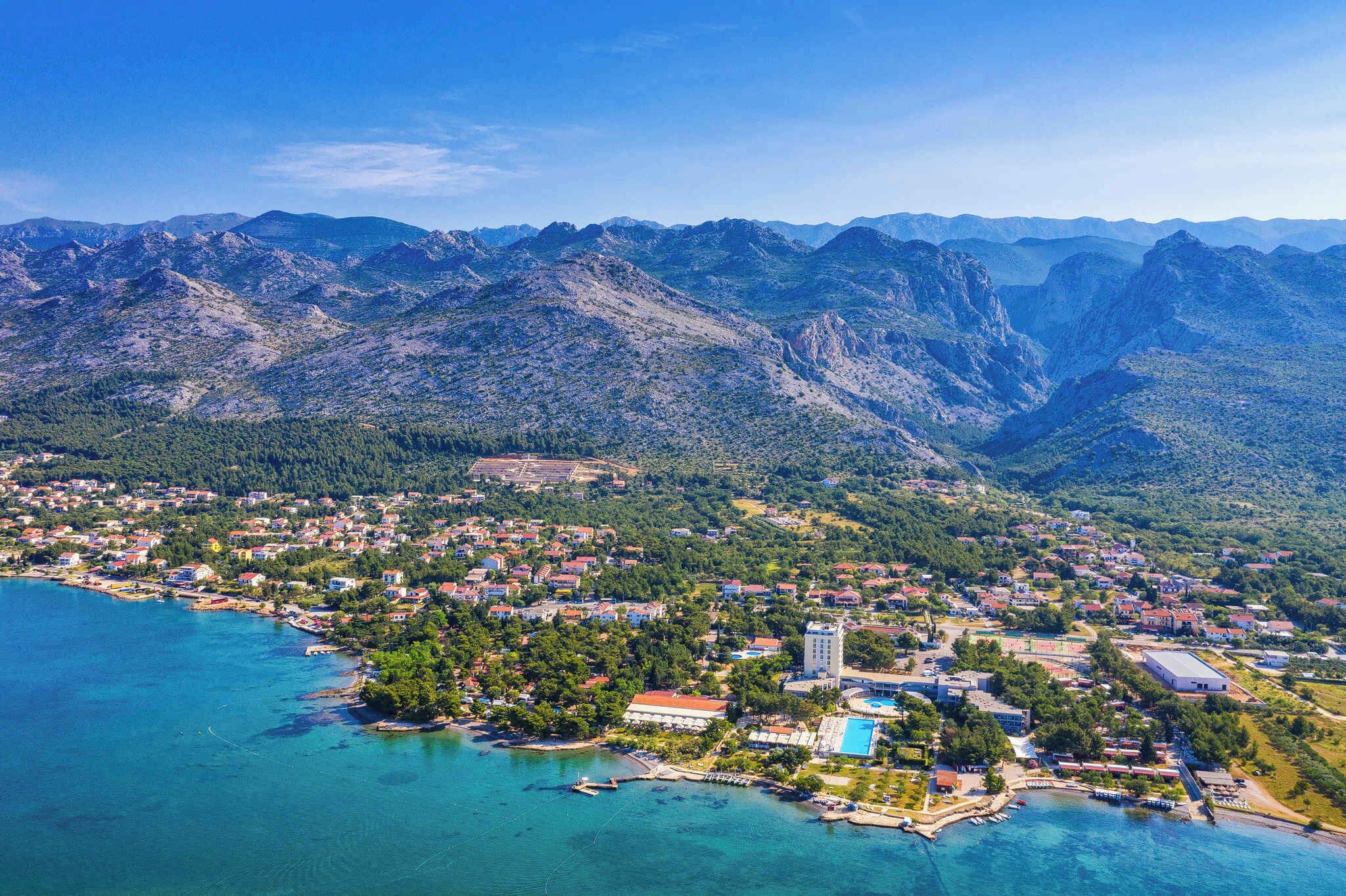 An aerial view of a coastal town with mountainous terrain in the background, a marina, and residential buildings.
