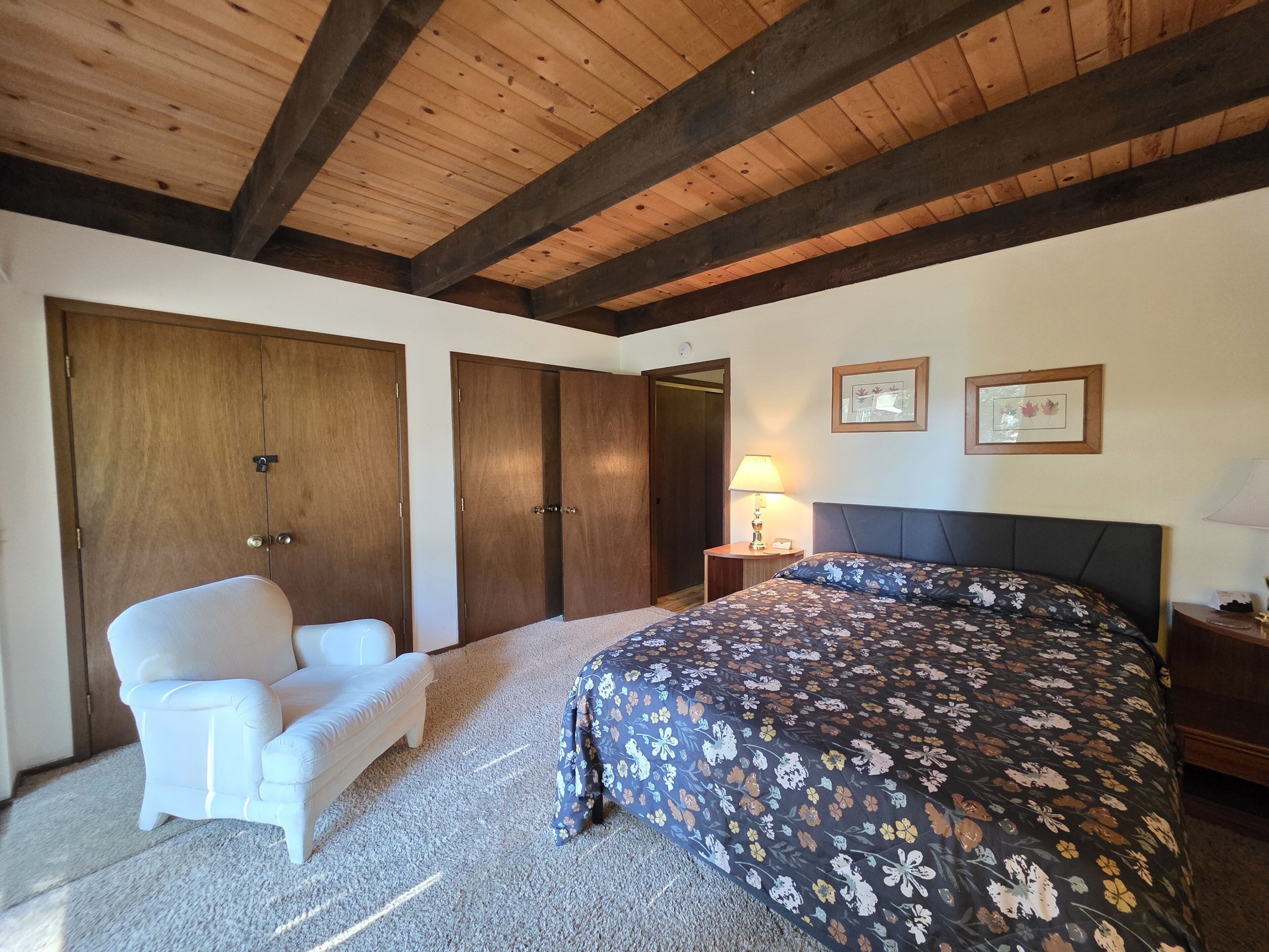 A bedroom with a bed, a chair, a nightstand, and wooden ceiling beams.
