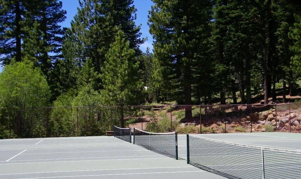 En utomhusbana för tennis omgiven av träd och en bergig sluttning.