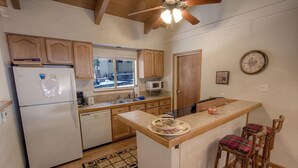 Cocina compacta con armarios de madera, microondas integrado y una pequeña isla con taburetes de bar.