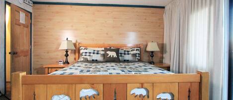 Una cama de madera con almohadas de motivos animales, una mesita de noche con una lámpara y una puerta con un cartel.