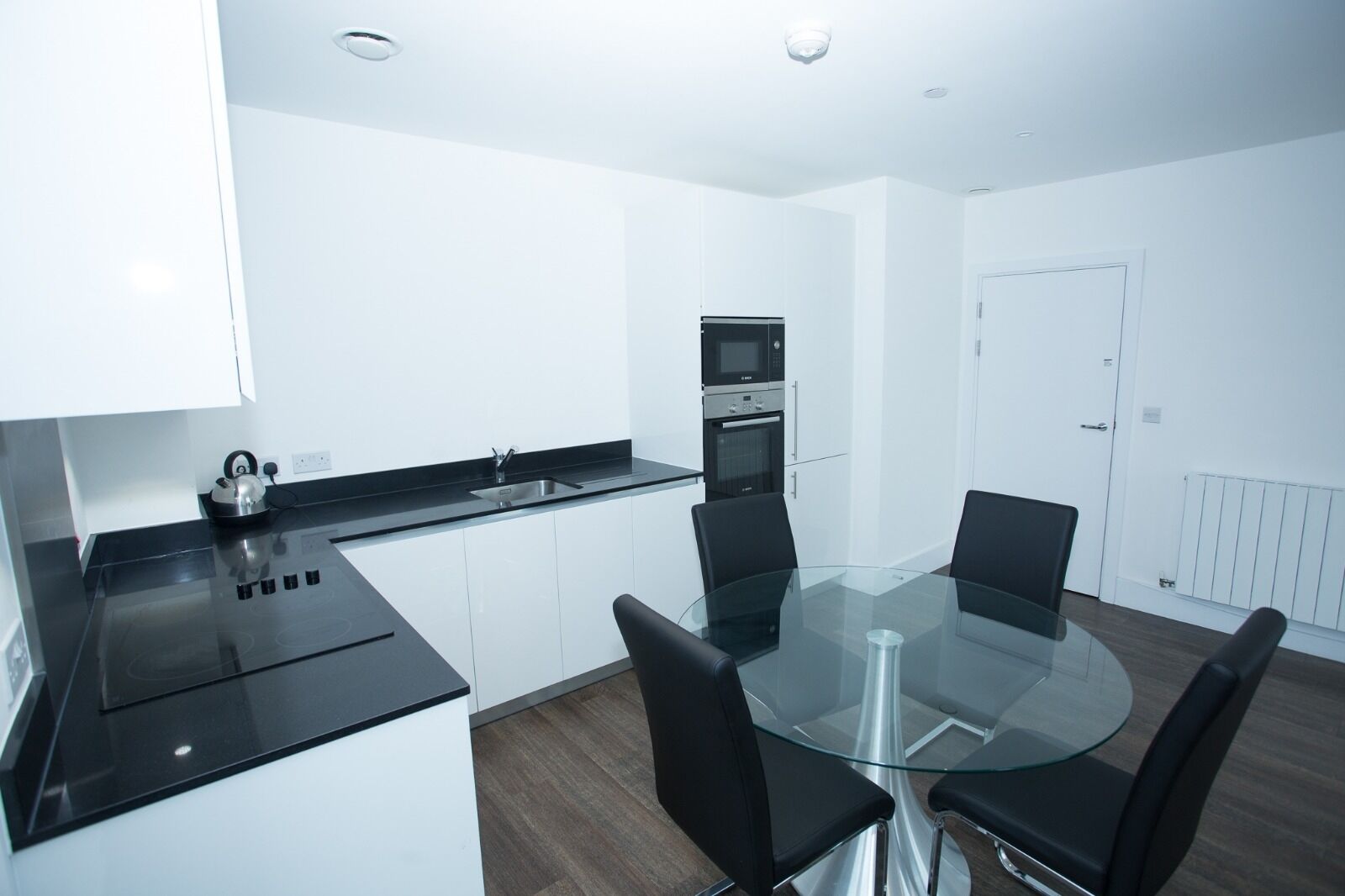 A modern kitchen with a black countertop, stainless steel appliances, and a glass dining table with four chairs.
