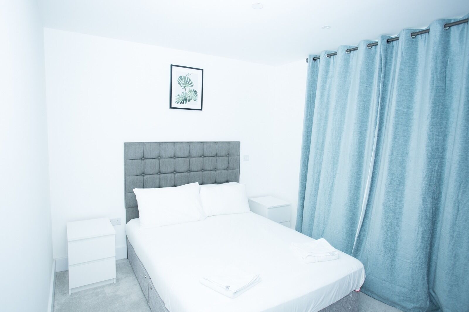 A neatly arranged bedroom with a tufted headboard, a single bed, a bedside table, and a nightstand.