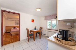 Une pièce compacte comprenant un lit, une petite table à manger avec des chaises, une machine à café et une fenêtre donnant sur des arbres.
