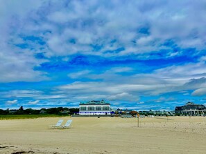 A beach with a large building in the background, a sandy beach area, and a clear sky with clouds.