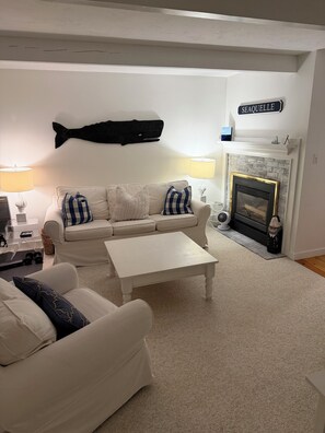 A living room with a white sofa, a coffee table, a fireplace, and a wall-mounted fish decoration.